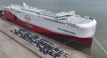Barco de transporte de vehículos BYD Zheng Zhou atracado en puerto con filas de coches eléctricos en el muelle, ilustrando la importación de vehículos y componentes desde China a Europa.